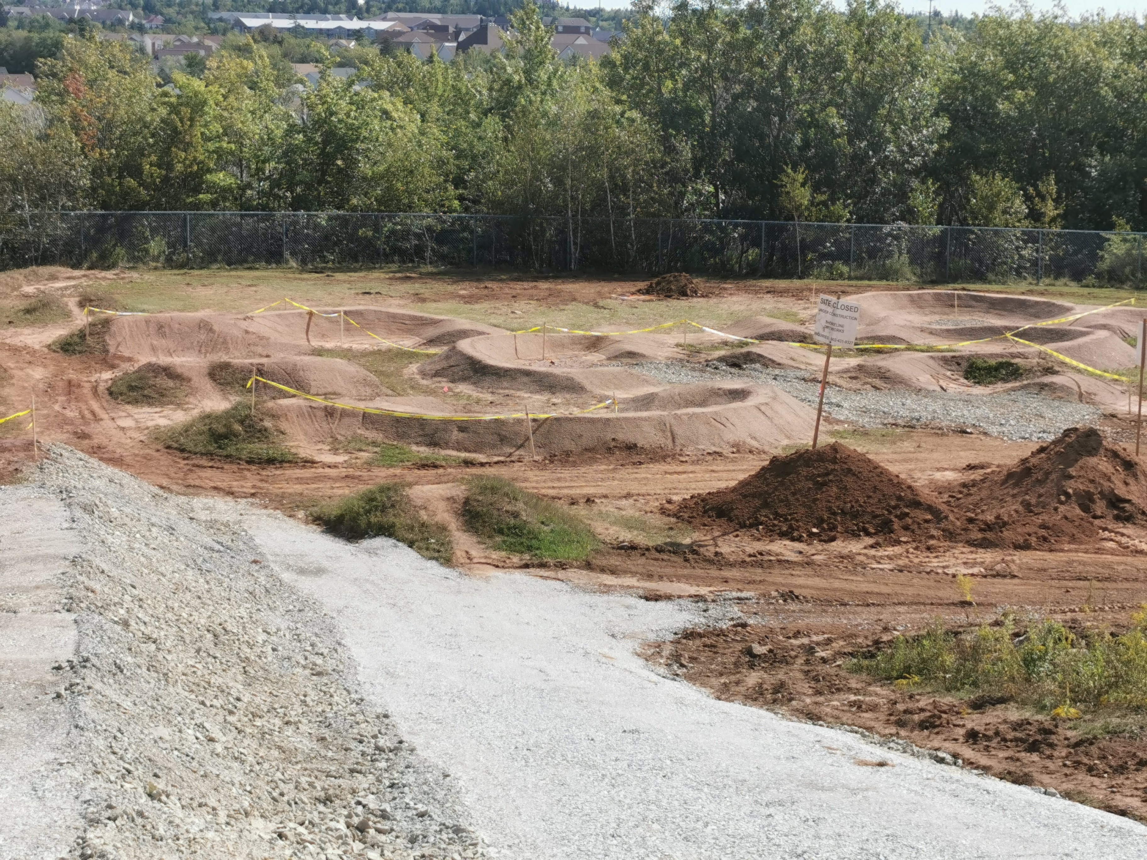 Pump track construction with gravel access and shaped riding features